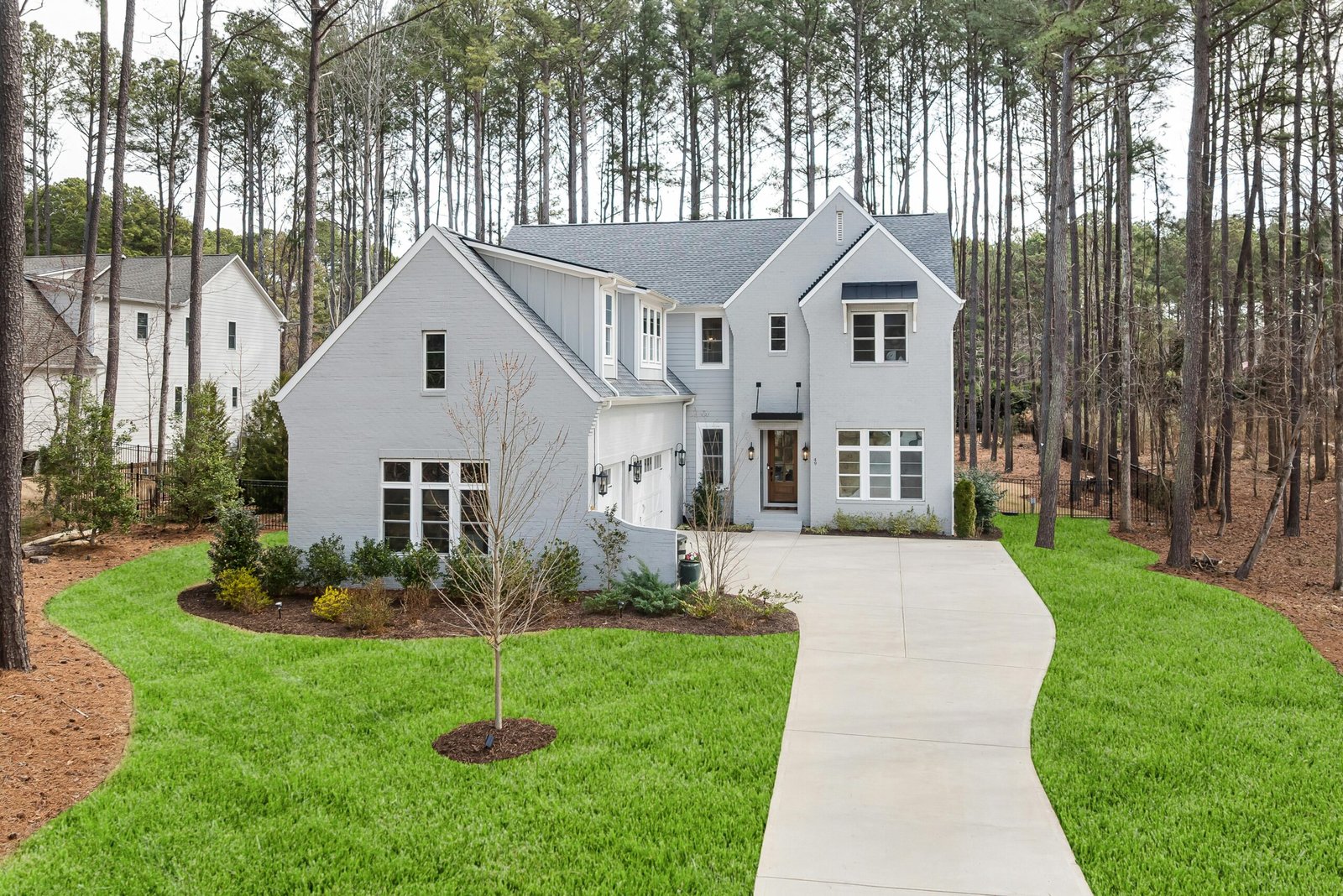 Elegant suburban home with gray siding and spacious driveway set amidst towering pine trees.